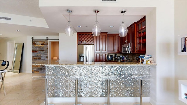 kitchen with visible vents, light stone countertops, a barn door, backsplash, and stainless steel appliances