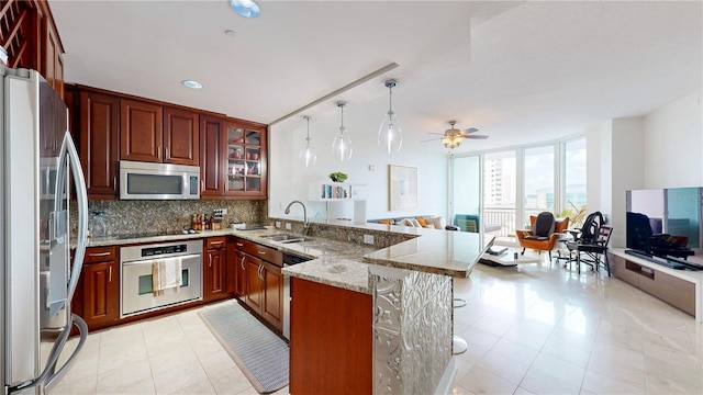 kitchen featuring a sink, stainless steel appliances, open floor plan, a peninsula, and glass insert cabinets