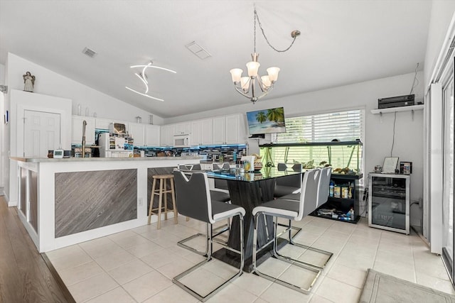 dining room with visible vents, lofted ceiling, beverage cooler, light tile patterned floors, and a notable chandelier