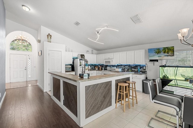 kitchen with visible vents, white cabinets, lofted ceiling, an inviting chandelier, and white appliances