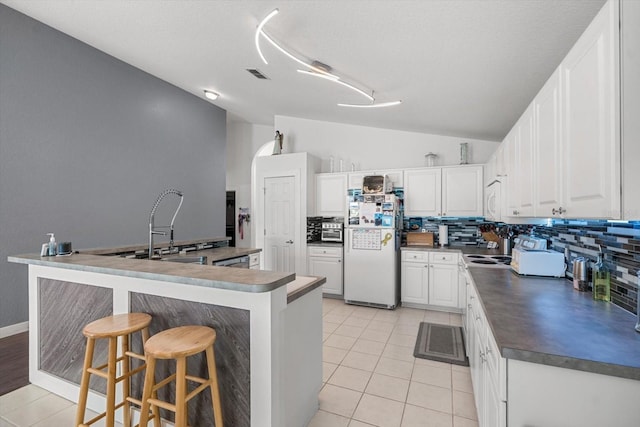 kitchen with visible vents, lofted ceiling, dark countertops, white appliances, and a kitchen bar