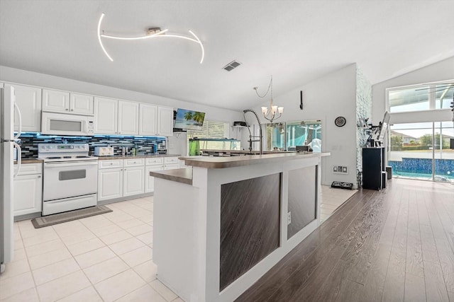 kitchen featuring white appliances, white cabinets, vaulted ceiling, and visible vents