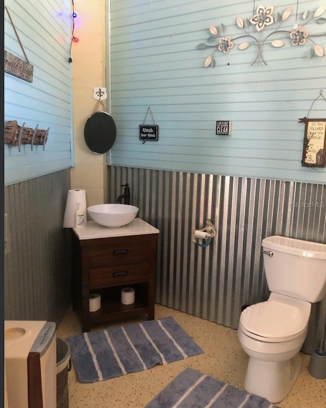 bathroom with wooden walls, toilet, and vanity