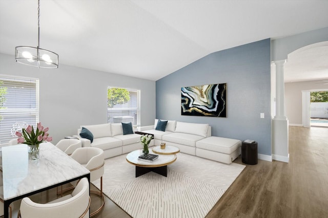 living room with wood finished floors, baseboards, a notable chandelier, lofted ceiling, and ornate columns