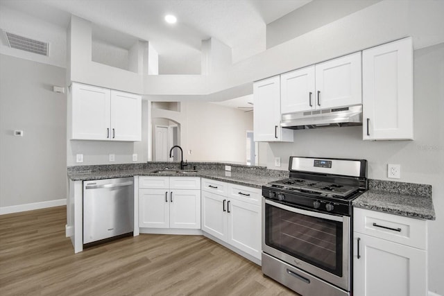 kitchen with appliances with stainless steel finishes, a sink, arched walkways, under cabinet range hood, and visible vents