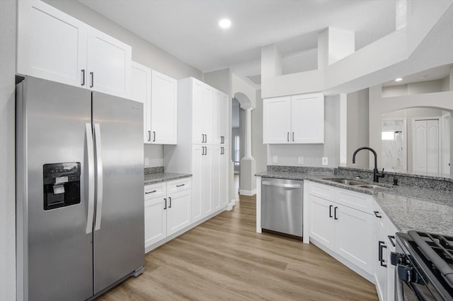 kitchen featuring white cabinets, light stone counters, a sink, arched walkways, and stainless steel appliances