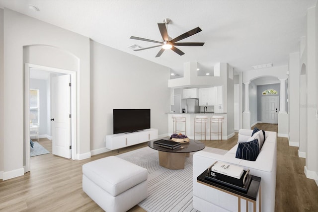 living room with a ceiling fan, visible vents, arched walkways, light wood finished floors, and ornate columns