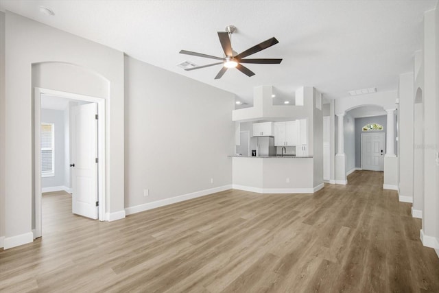 unfurnished living room featuring light wood-style floors, arched walkways, a ceiling fan, ornate columns, and visible vents