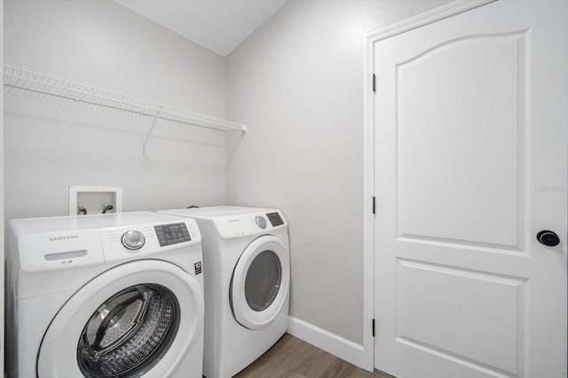 laundry area with laundry area, washer and clothes dryer, baseboards, and wood finished floors