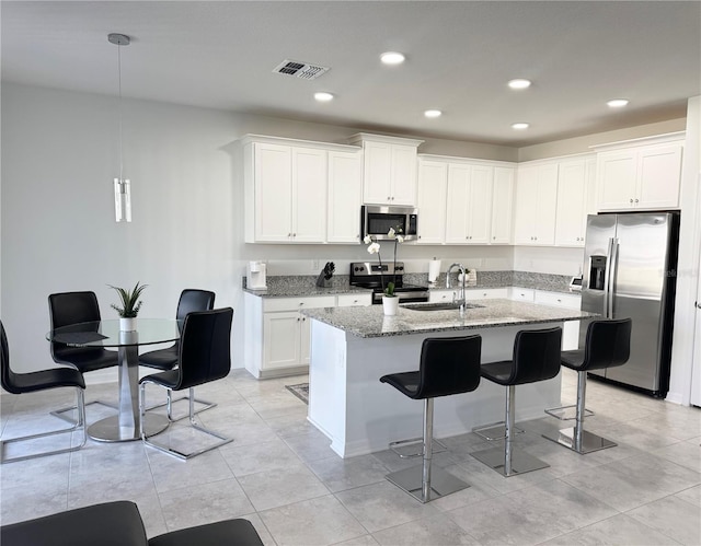 kitchen featuring light stone countertops, a kitchen island with sink, stainless steel appliances, a kitchen bar, and visible vents