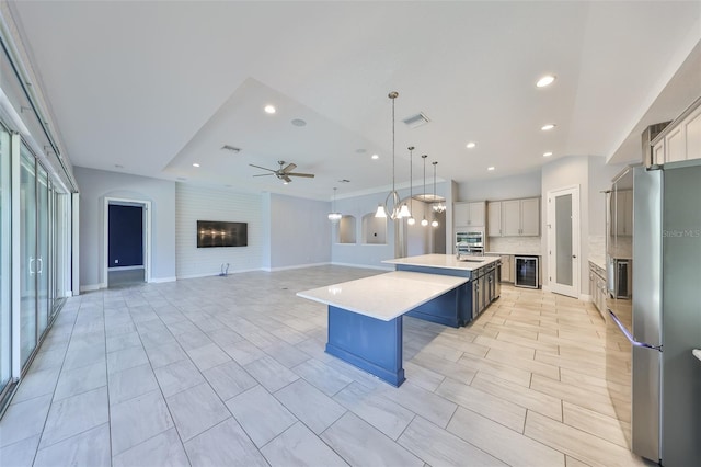 kitchen with a kitchen island with sink, a fireplace, beverage cooler, ceiling fan, and appliances with stainless steel finishes