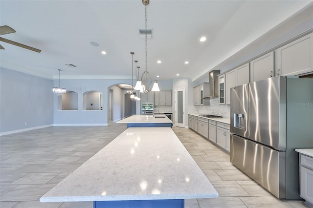 kitchen with wall chimney range hood, crown molding, a kitchen island with sink, stainless steel appliances, and gray cabinetry