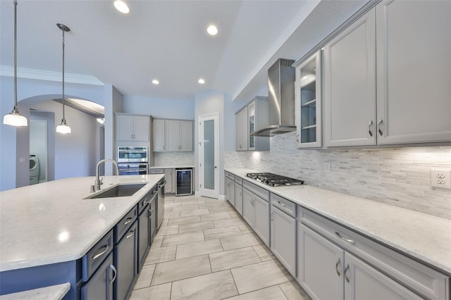 kitchen with wall chimney range hood, appliances with stainless steel finishes, tasteful backsplash, a sink, and beverage cooler