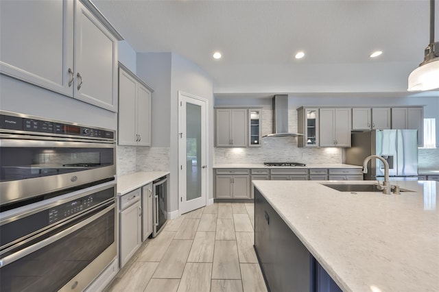 kitchen with gray cabinetry, appliances with stainless steel finishes, beverage cooler, and wall chimney exhaust hood
