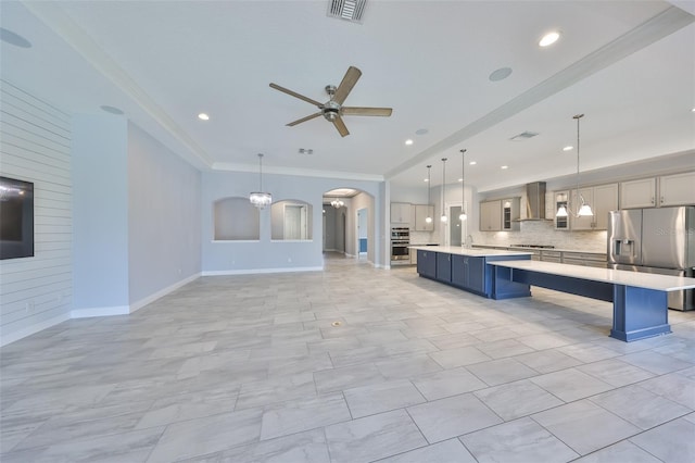 kitchen featuring light countertops, arched walkways, wall chimney exhaust hood, ceiling fan with notable chandelier, and stainless steel appliances