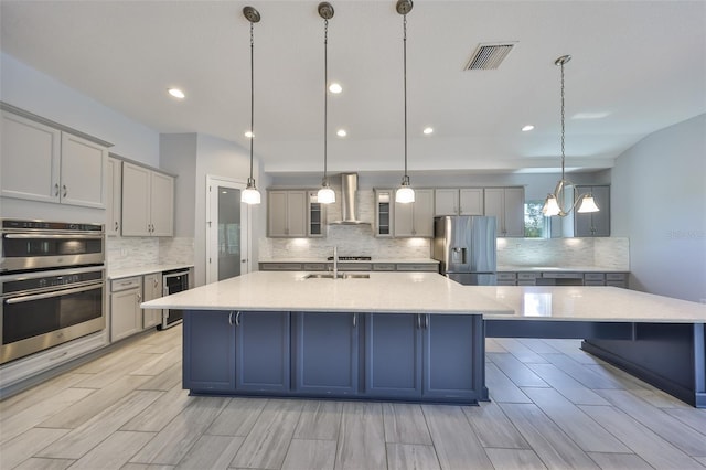 kitchen featuring wall chimney range hood, backsplash, visible vents, beverage cooler, and stainless steel appliances