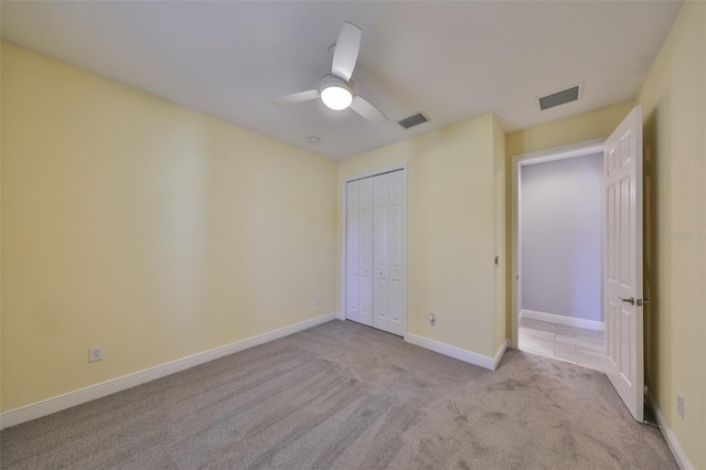 unfurnished bedroom featuring light colored carpet, a ceiling fan, visible vents, and a closet