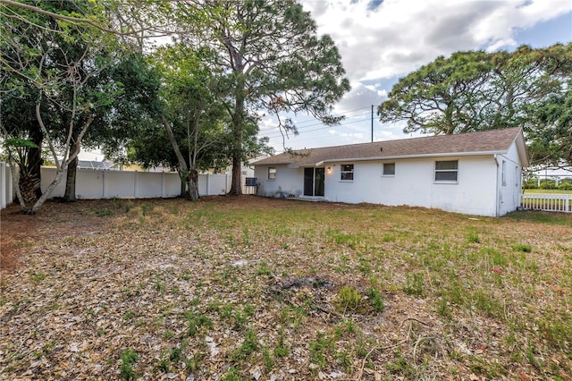 rear view of property with fence, a shingled roof, and concrete block siding