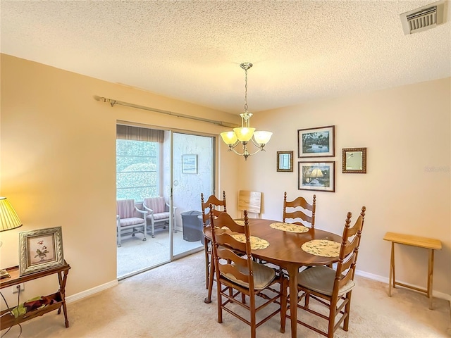 dining room featuring a textured ceiling, light colored carpet, visible vents, baseboards, and a chandelier