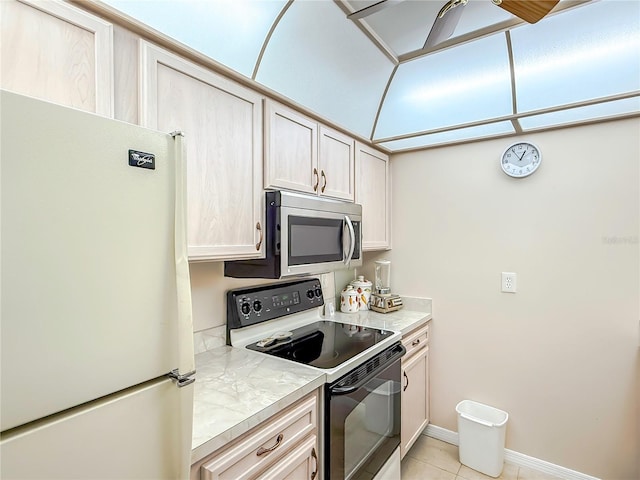 kitchen featuring freestanding refrigerator, stainless steel microwave, a ceiling fan, light tile patterned floors, and range with electric cooktop