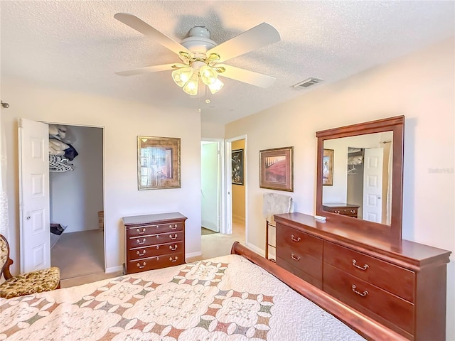 bedroom with a walk in closet, a ceiling fan, a textured ceiling, visible vents, and carpet flooring