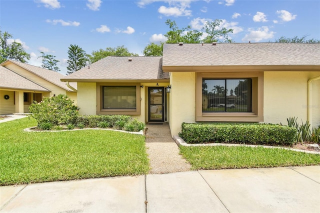 ranch-style home with a shingled roof, stucco siding, and a front lawn
