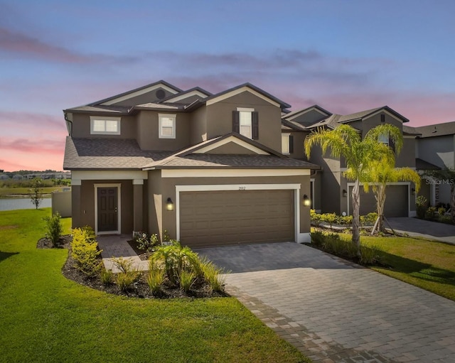 traditional home featuring a front yard, a garage, decorative driveway, a shingled roof, and stucco siding
