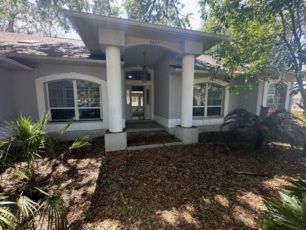 6433 Brentwood Dr, Zephyrhills, FL 33542 - view of exterior entry featuring roof with shingles and stucco siding