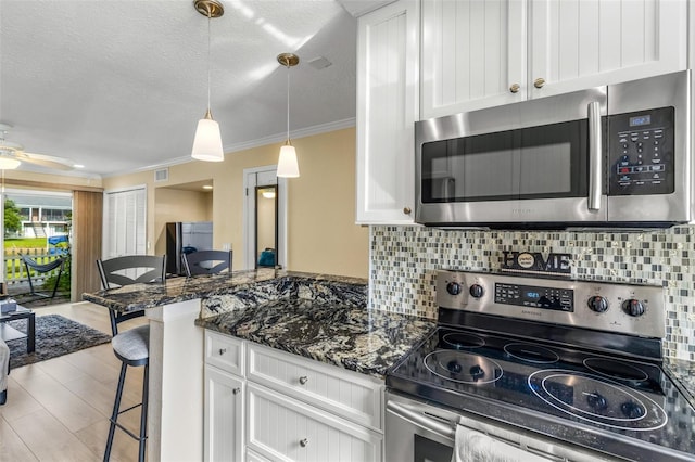 kitchen with a kitchen bar, white cabinets, tasteful backsplash, a ceiling fan, and appliances with stainless steel finishes