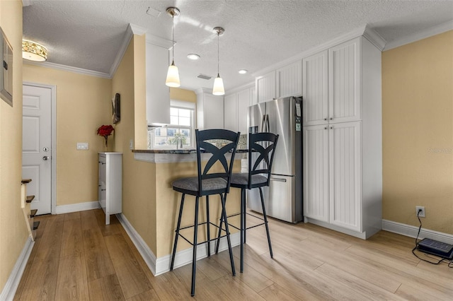 kitchen featuring freestanding refrigerator, light wood-style flooring, a kitchen breakfast bar, and ornamental molding