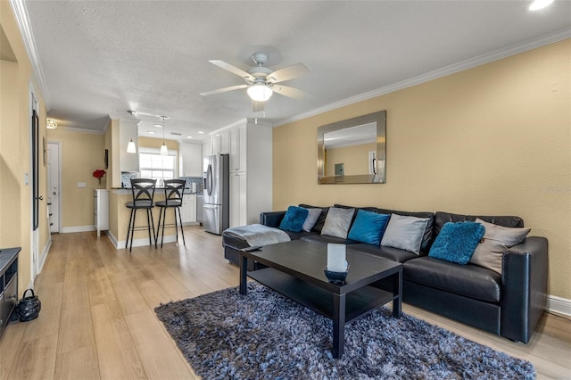 living area featuring light wood-style floors, baseboards, ceiling fan, and ornamental molding