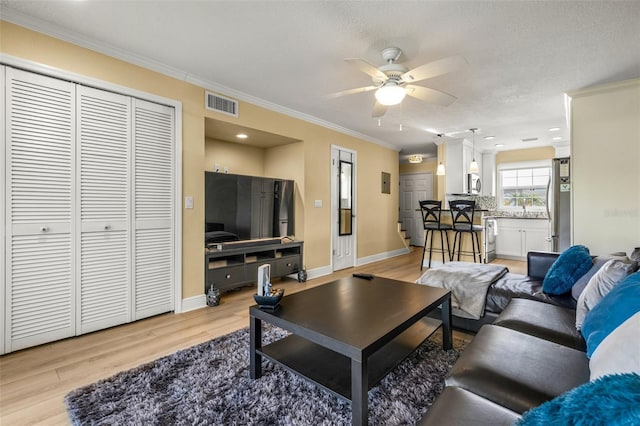 living room with crown molding, ceiling fan, light wood-style flooring, baseboards, and visible vents
