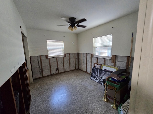 unfurnished room with speckled floor, ceiling fan, a wealth of natural light, and a wainscoted wall