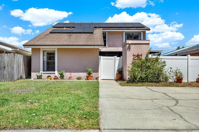 mid-century home featuring roof mounted solar panels, stucco siding, a front yard, and fence