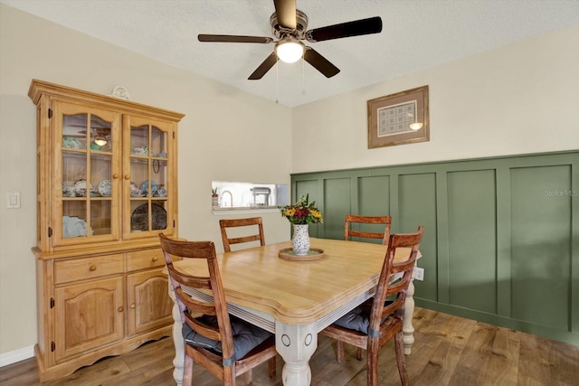 dining space featuring light wood-style floors, a wainscoted wall, ceiling fan, and a decorative wall