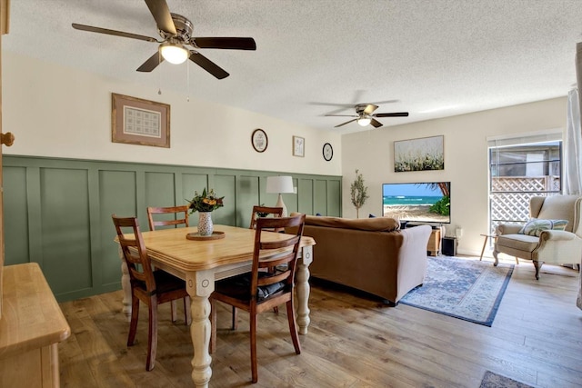 dining area with ceiling fan, a decorative wall, light wood finished floors, and a textured ceiling