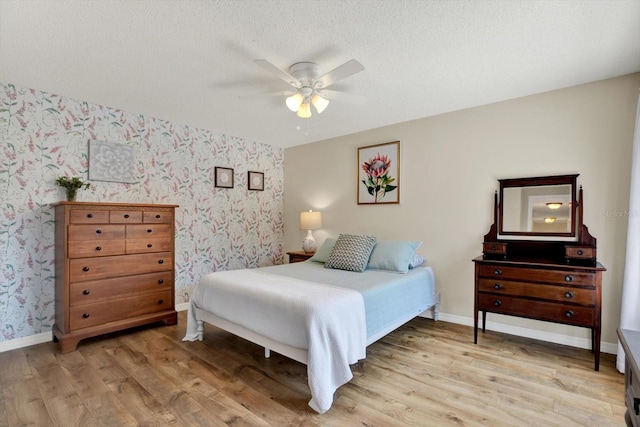 bedroom with ceiling fan, light wood finished floors, a textured ceiling, wallpapered walls, and baseboards