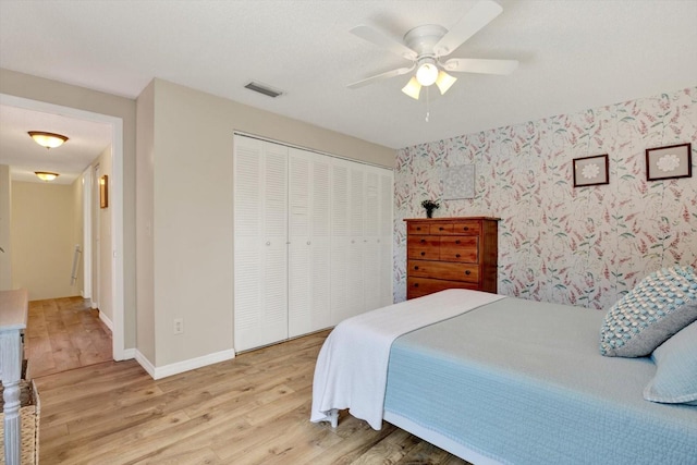 bedroom featuring ceiling fan, visible vents, light wood-type flooring, baseboards, and a closet