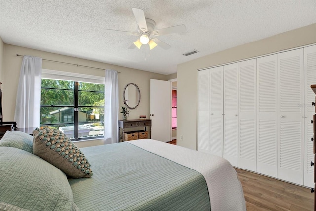 bedroom with ceiling fan, a textured ceiling, visible vents, and wood finished floors