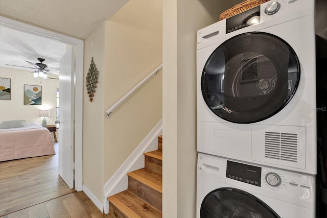 washroom featuring ceiling fan, stacked washer / drying machine, wood finished floors, and laundry area