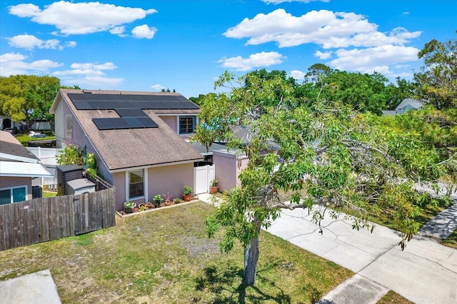view of front facade with fence, a shingled roof, stucco siding, a front yard, and roof mounted solar panels