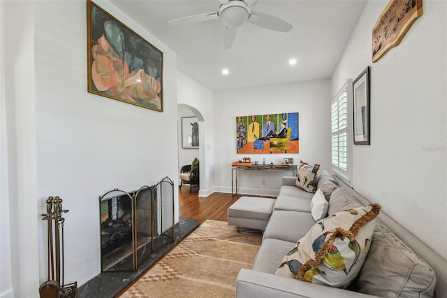 living room featuring a ceiling fan, arched walkways, wood finished floors, baseboards, and recessed lighting