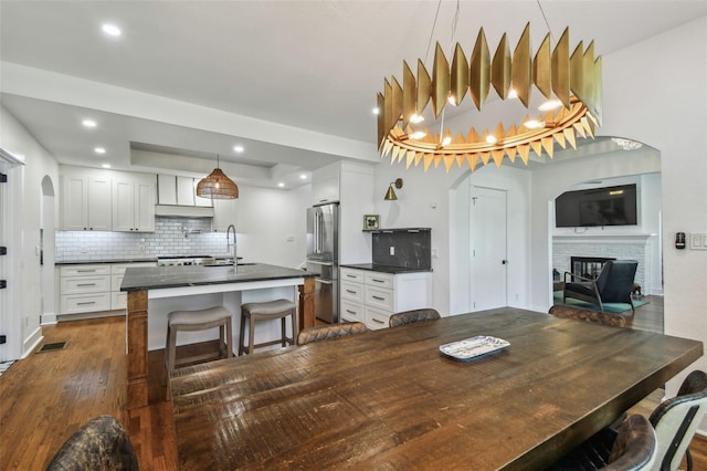 dining area featuring visible vents, a glass covered fireplace, dark wood-style floors, recessed lighting, and arched walkways