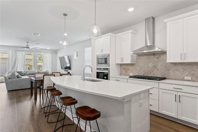 kitchen with wall chimney range hood, a sink, dark wood finished floors, appliances with stainless steel finishes, and backsplash