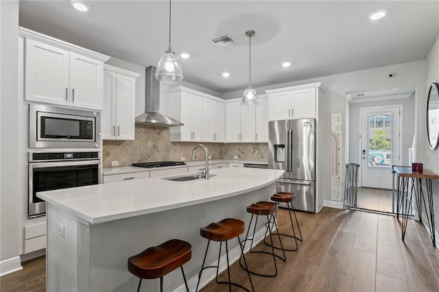 kitchen featuring wall chimney range hood, appliances with stainless steel finishes, a sink, dark wood-type flooring, and visible vents