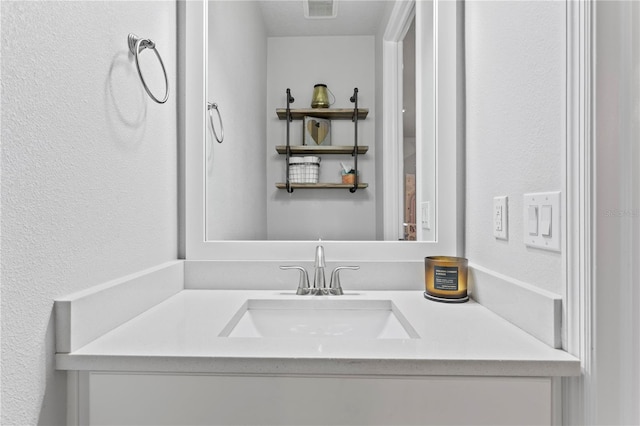 bathroom with a textured wall, visible vents, and vanity