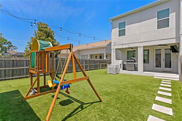 view of playground with a fenced backyard, a ceiling fan, a lawn, and french doors