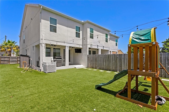 back of house with a fenced backyard, a playground, a yard, a patio, and stucco siding