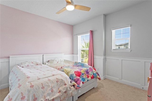 bedroom featuring carpet flooring, a ceiling fan, wainscoting, and a decorative wall