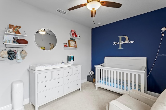 bedroom featuring a ceiling fan, visible vents, a nursery area, baseboards, and light carpet